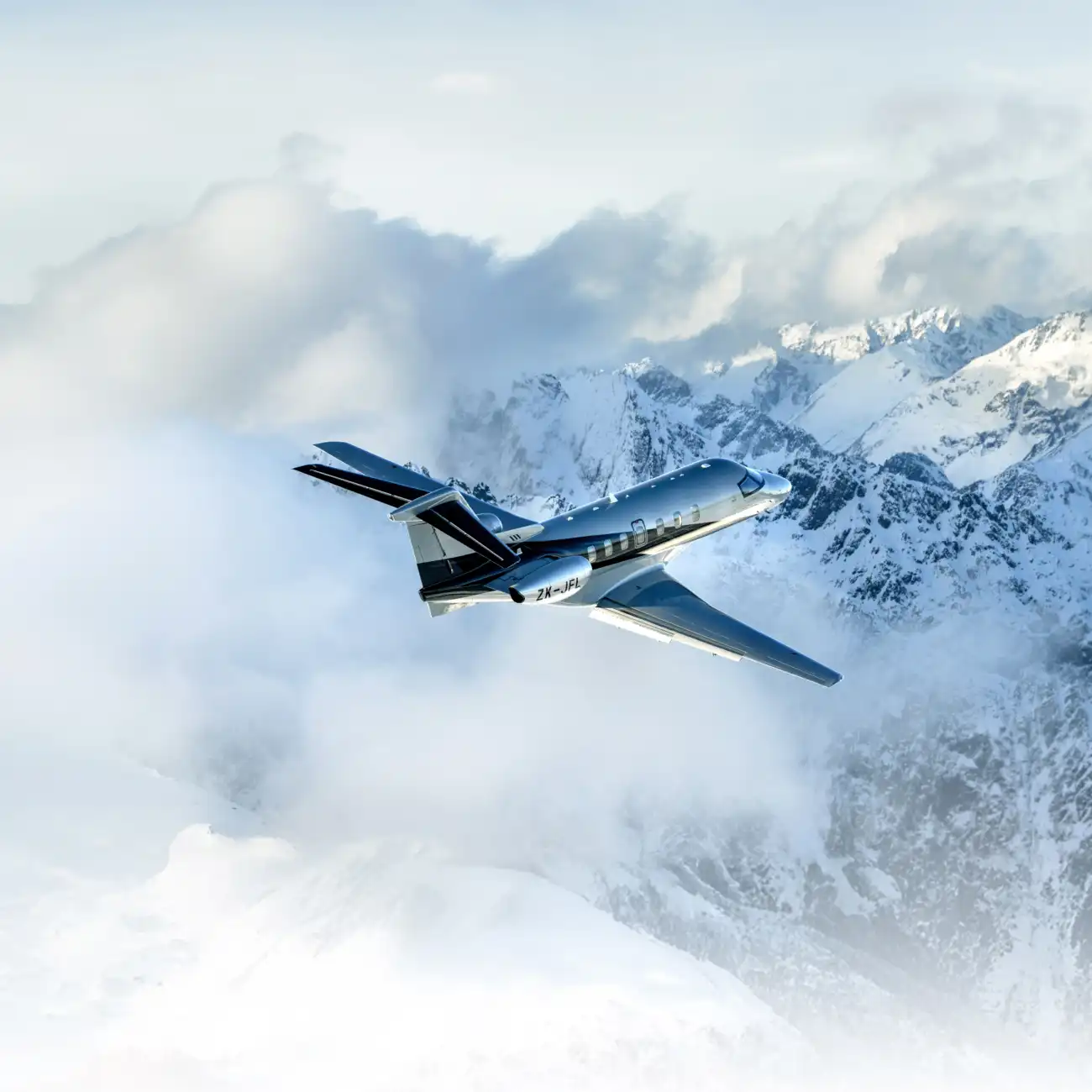 A PC-24 flies over snow-covered mountains in New Zealand, with mist surrounding the landscape