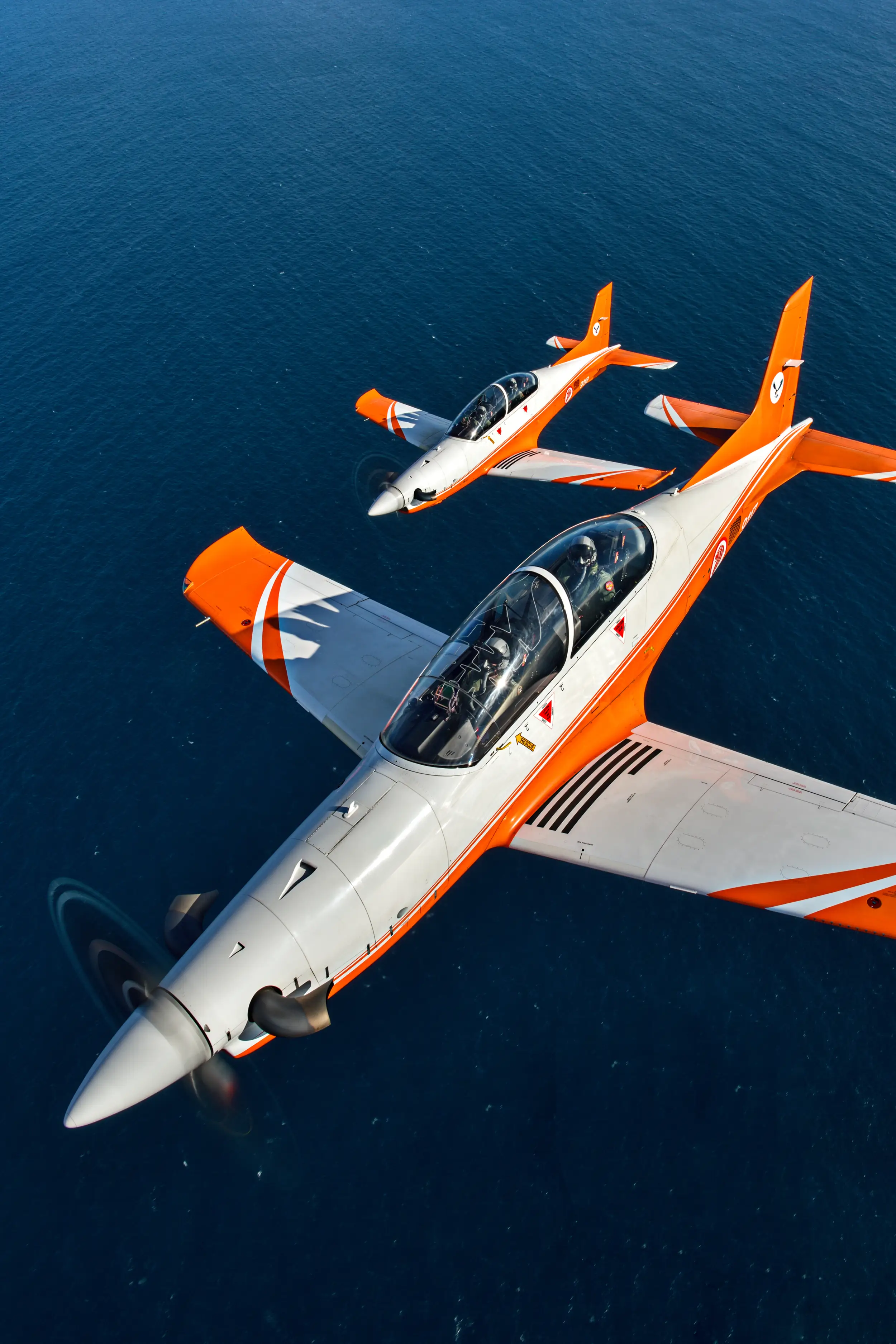 Two PC-21 aircraft of the Singapore Air Force fly over the water.
