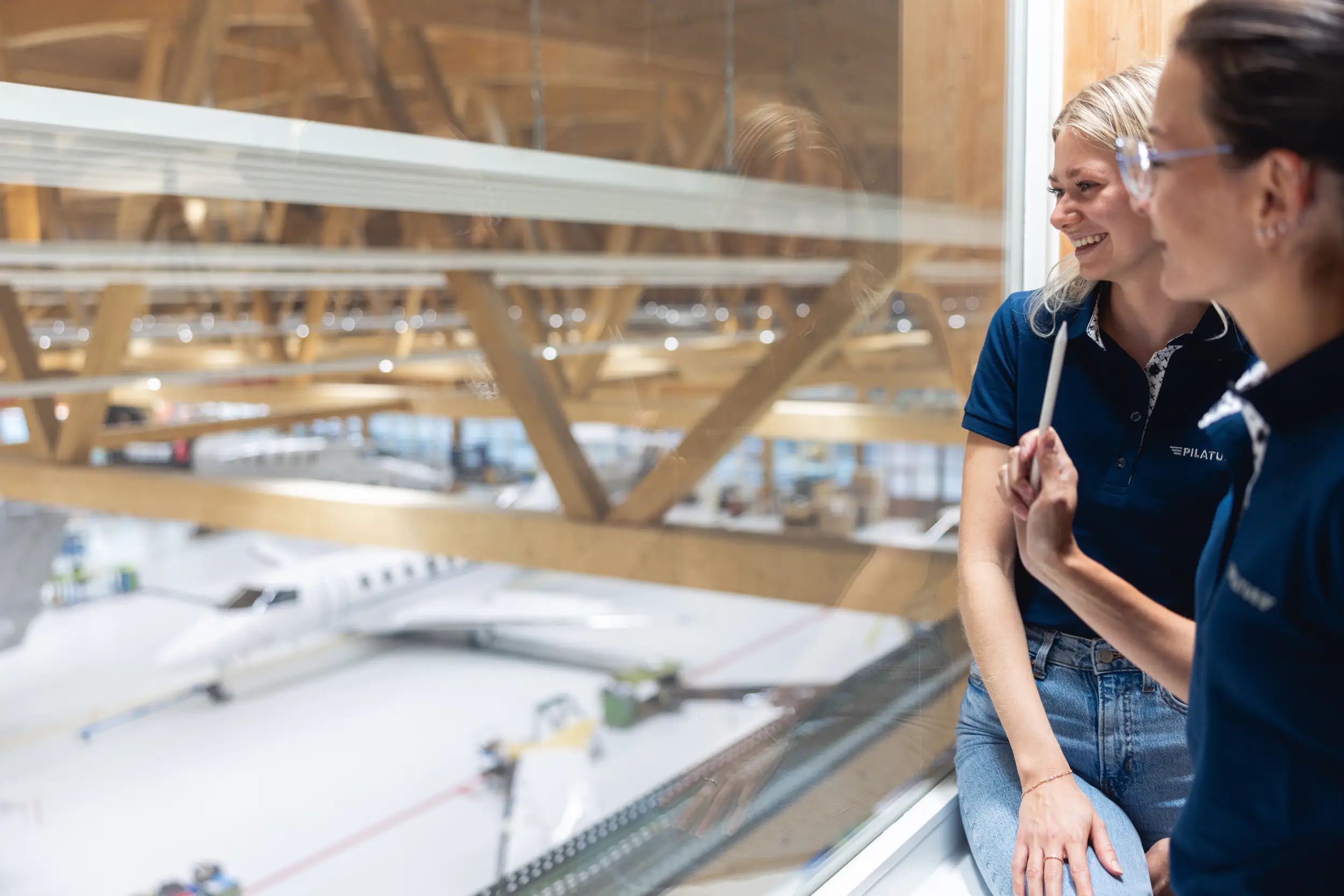 Two employees are talking while looking down at airplanes in the hangar.
